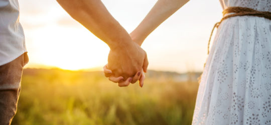 Couple,Hold,Hands,In,Green,Field,On,Sunset